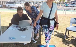 Dr Sophie Scamps MP takes great interest in Abishek Shrestha's work testing balance for World CEP Day at Dee Why Beach.